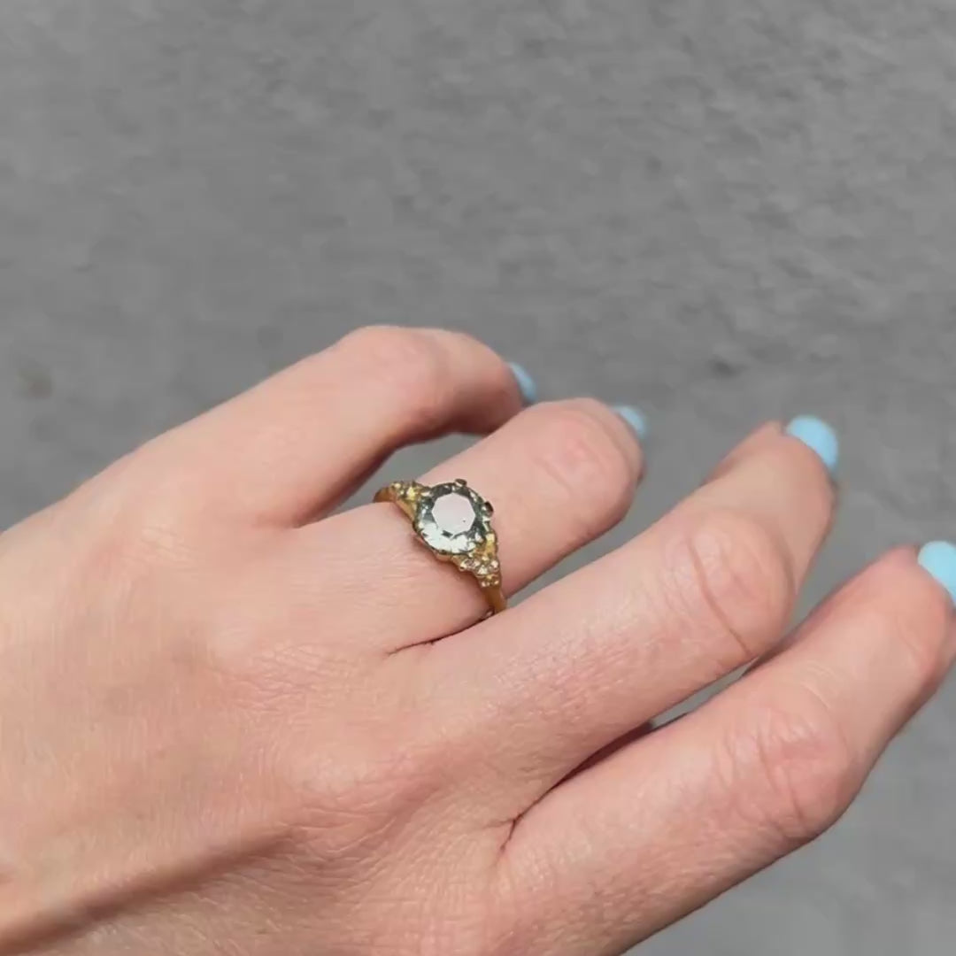 Hand wearing a Johnny Ninos gold ring with a green gemstone against a gray background