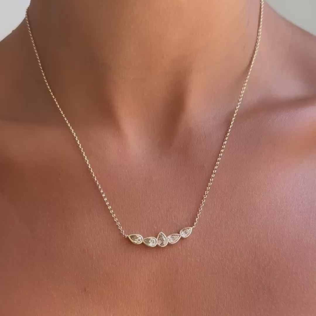 A delicate gold chain necklace with five small champagne diamonds worn on a model's neck.