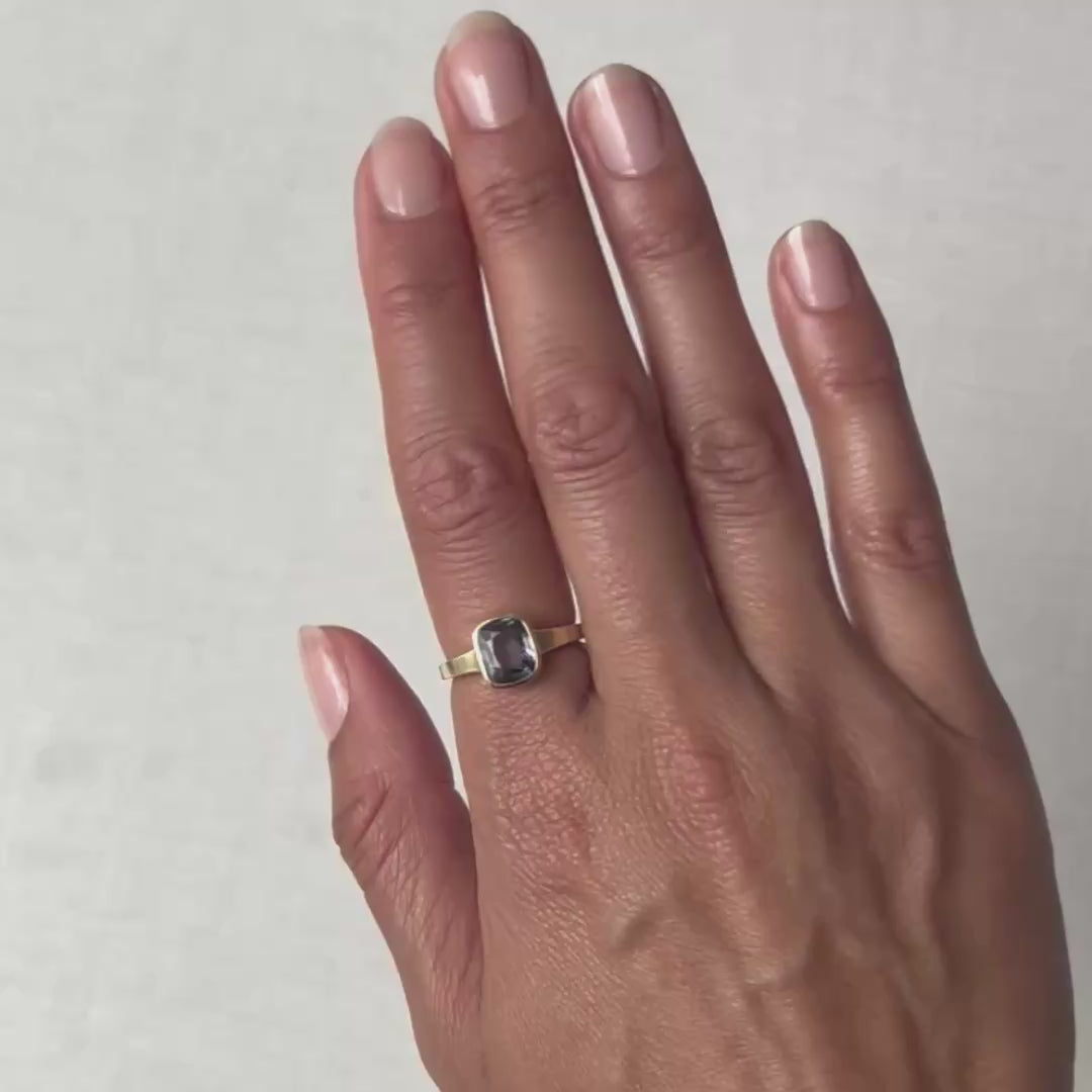 A close-up of a hand wearing a gold ring with a rectangular blue gemstone.
