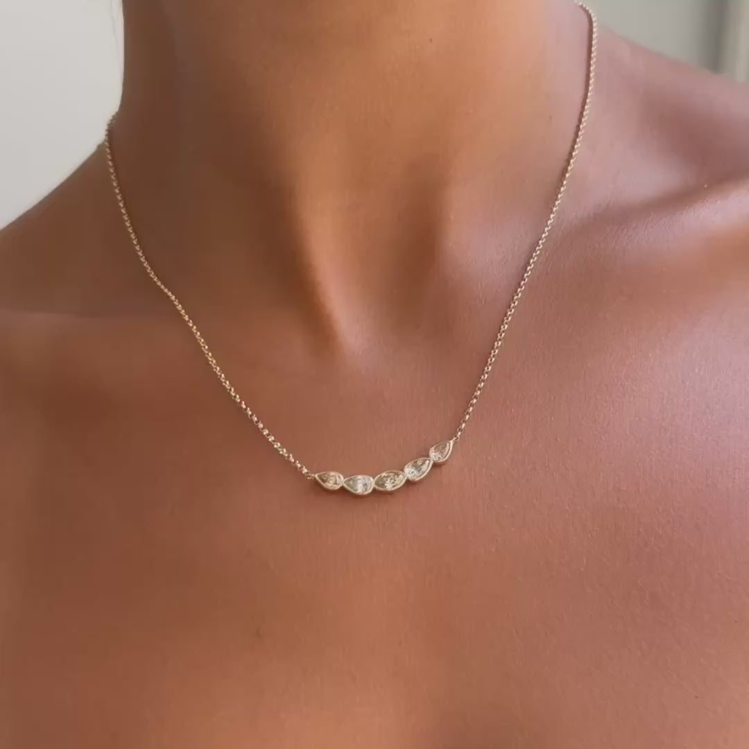 A delicate gold chain necklace with five small, irregularly shaped clear diamonds, shown worn on a model's neck.