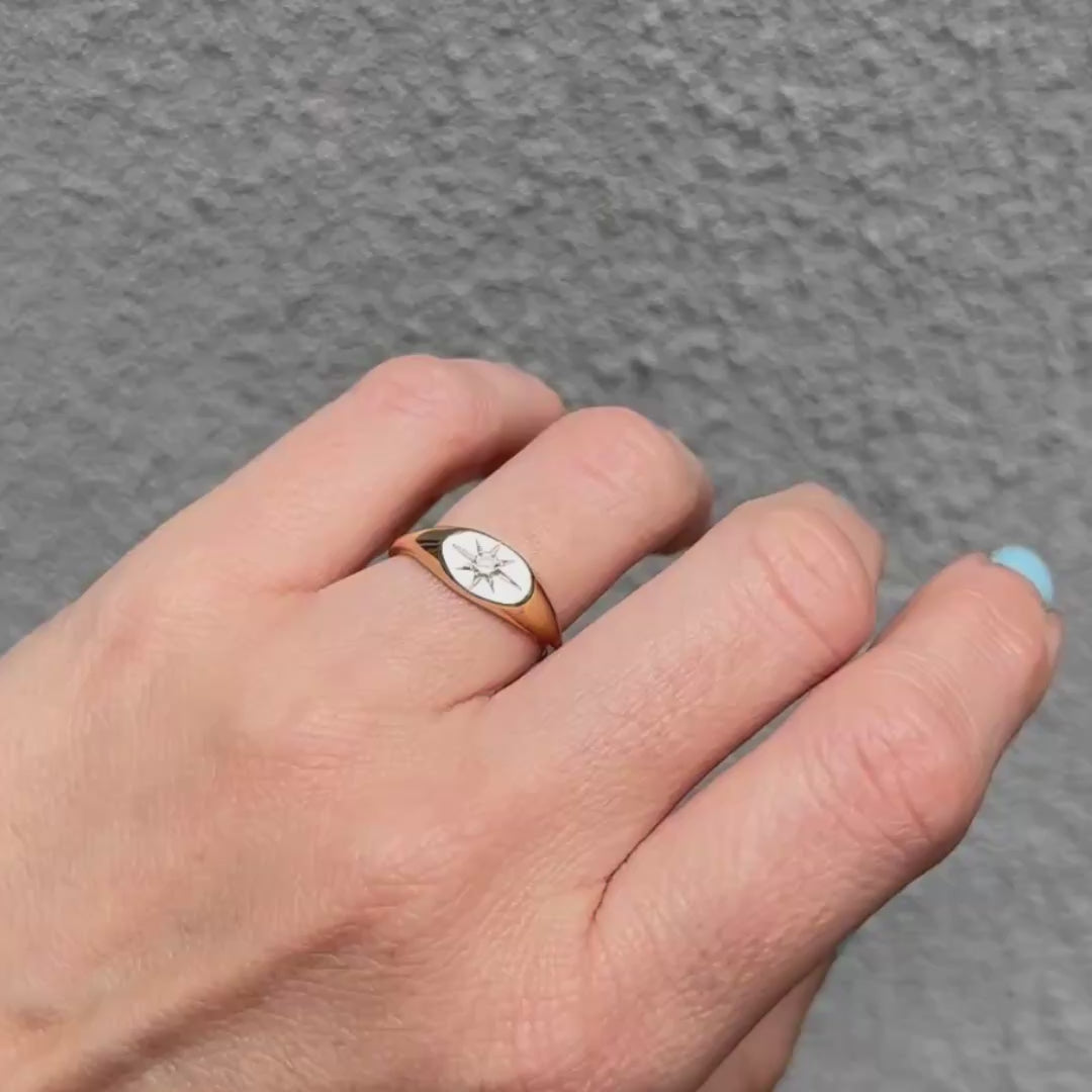 Gold ring with a star design on a person's finger against a gray background