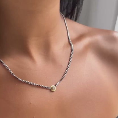 A close-up of a model's neck and upper chest wearing a delicate silver chain necklace with a small gold and diamond pendant.
