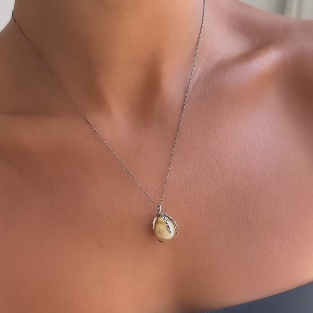 A close-up of a person wearing a delicate silver chain necklace with a single round, cream-colored pearl pendant, styled with a black strapless top.