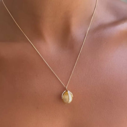 A close-up of a model's chest wearing a delicate gold chain necklace with a pearl, textured gold pendant.